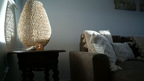 A room with a woven lamp on a wooden table, a sofa with a white blanket, and a painting on the wall. - Carvoeiro Sol Right by the sea (Carvoeiro)