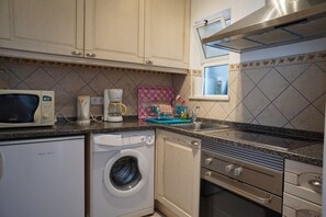 A compact kitchen with a microwave, coffee maker, washing machine, and a small window. - Carvoeiro Sol Right by the sea (Carvoeiro)
