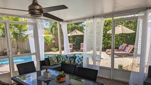 Un patio techado con una mesa de vidrio, sillas y un ventilador de techo.
