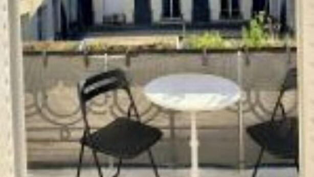 A balcony with two chairs and a small round table, overlooking a row of buildings with white facades and dark roofs. - Home Sweet Home Claridge Champs-Elysées (Paris)