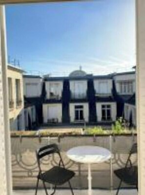 A balcony with two chairs and a small round table, overlooking a row of buildings with white facades and dark roofs.