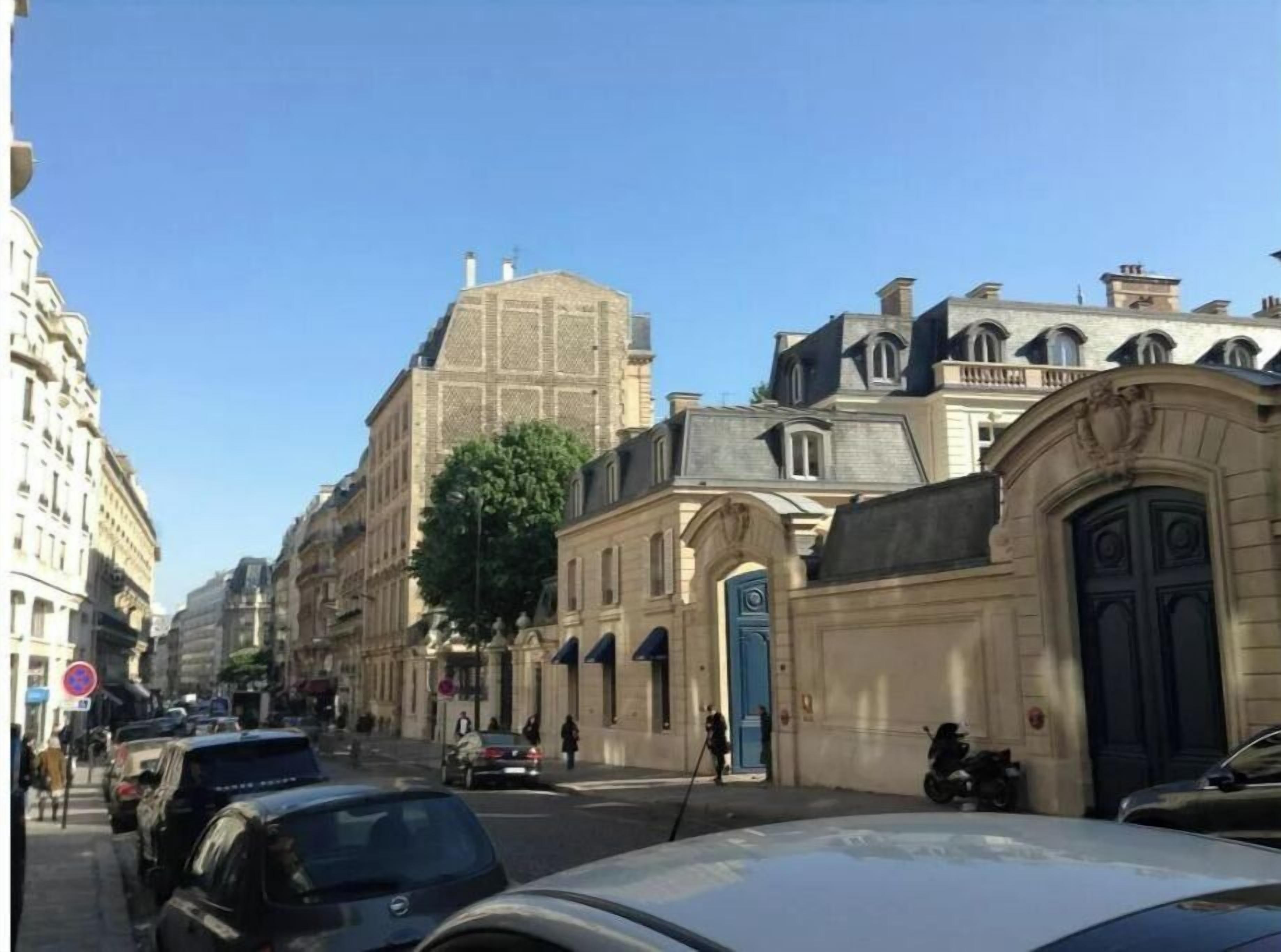 A street with historic buildings, parked cars, and a clear blue sky.