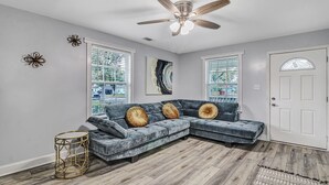 A modern living room with a sectional sofa, a ceiling fan, and a large window with blinds. - 5 minutes drive to downtown Savannah. (Savannah)