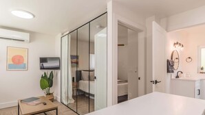 A modern bedroom with a bed, a bedside table, a TV, and a sliding door leading to a bathroom.