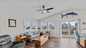 A spacious living room with a ceiling fan, two sofas, a coffee table, and a large window with blinds.