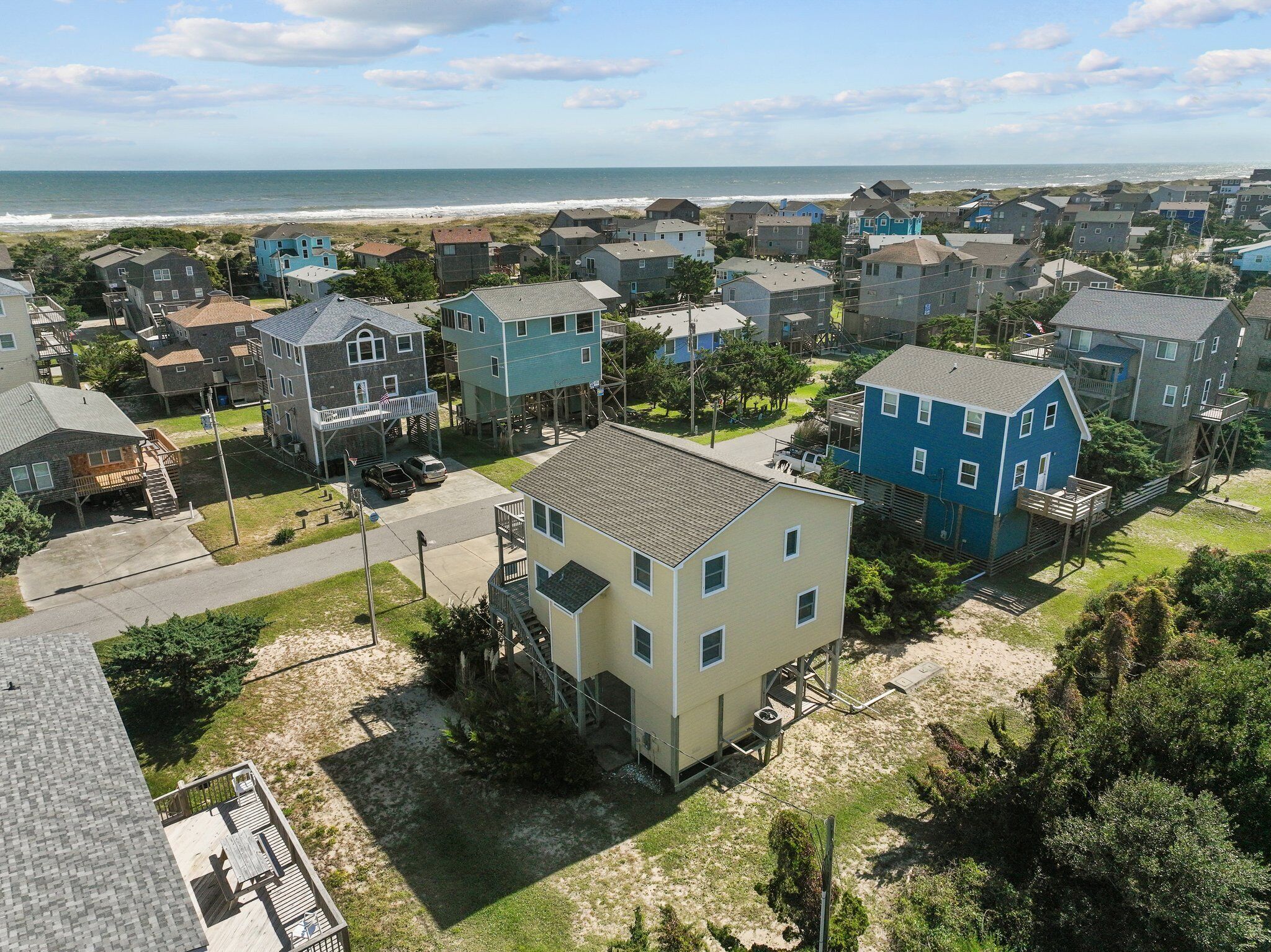 A coastal residential area with houses, some elevated on stilts, and a beach in the background.