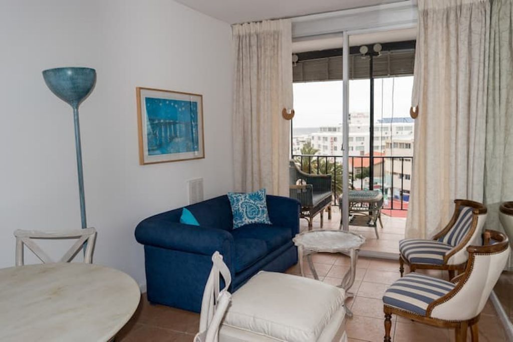 A living room with a blue sofa, white armchairs, a small table, and a floor lamp.
