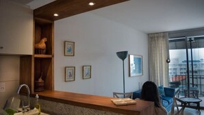 Ein modernes Wohnzimmer mit einem Holzbüro, einer Couch und einem Esstisch. An der Wand hängen gerahmte Bilder und ein großes Fenster mit Blick auf Gebäude.