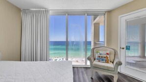 A hotel room with a large bed, a chair with a beach-themed pillow, and a balcony with a view of the beach and ocean. - ☀️Gulf Front, Amazing Views-Long Beach Resort 1-1203☀️ (Panama City Beach)