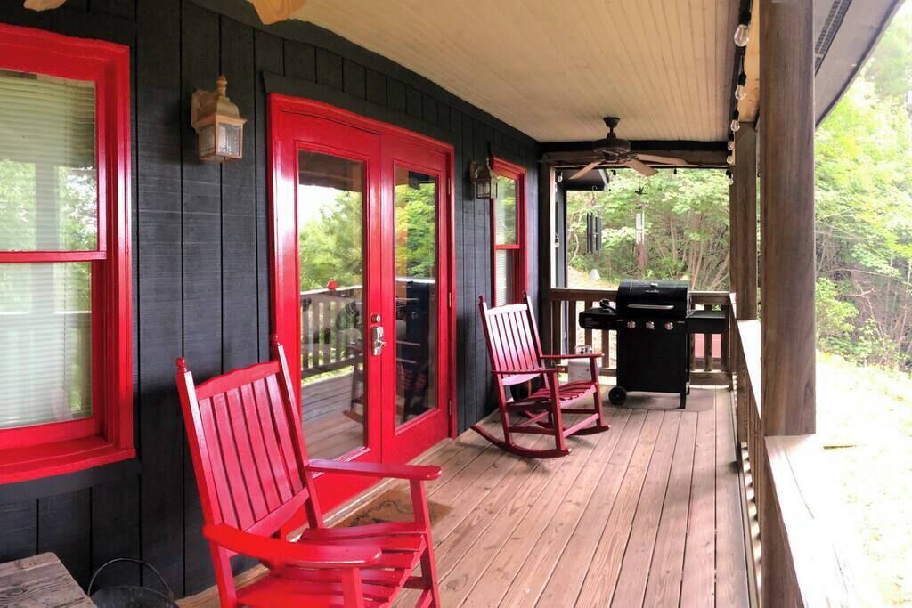 A porch with red-framed doors, a grill, and rocking chairs.