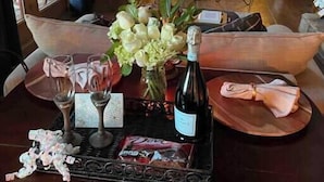 Un coin repas avec une table dressée pour deux personnes, agrémenté d’une bouteille de vin, de verres et d’un menu.
