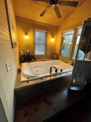 A wooden cabin bathroom with a large bathtub, wooden walls, and two windows. - Beardsicle Bluff Cabin (Chatsworth)