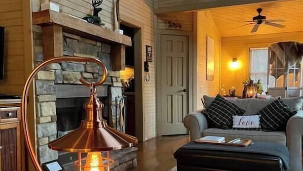 Un salon chaleureux avec une cheminée en pierre, un lampadaire moderne et un coin salon confortable comprenant un canapé et un pouf.