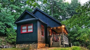 Une cabane dotée d’une véranda, de fondations en pierre et d’un petit espace extérieur aménagé pour s’asseoir.