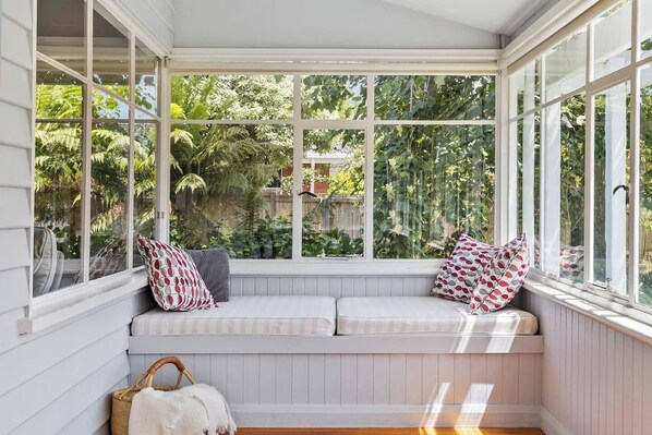 A cozy reading nook with a cushioned bench, a wicker basket, and a view of lush greenery outside.