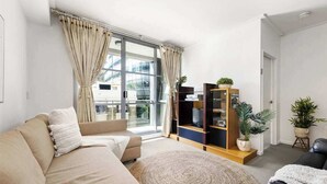 A modern living room with a beige sofa, a round woven rug, and a wooden entertainment unit with plants. - A Stylish Apt for 6 Right Next to Darling Harbour (Sydney)