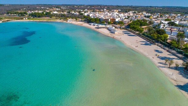 Eine Luftaufnahme einer Küstenstadt mit sandigem Strand, klarem türkisblauem Wasser und Wohngebäuden.