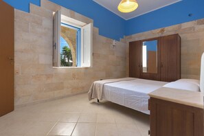Ein Zimmer mit zwei Betten, einem Holzschrank, einem großen Spiegel und einem Fenster mit geöffneter Tür.