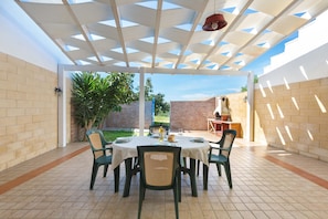 Eine Terrasse im Freien mit überdachtem Essbereich, Ziegelmauern und Blick auf den Garten.