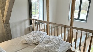 Ein Schlafzimmer mit einem Holzbett, weißer Bettwäsche und Blick ins Freie durch ein Fenster.