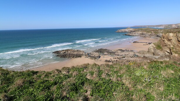 A coastal landscape with rocky cliffs, a sandy beach, and a clear blue sky. - Dunes View (Newquay)