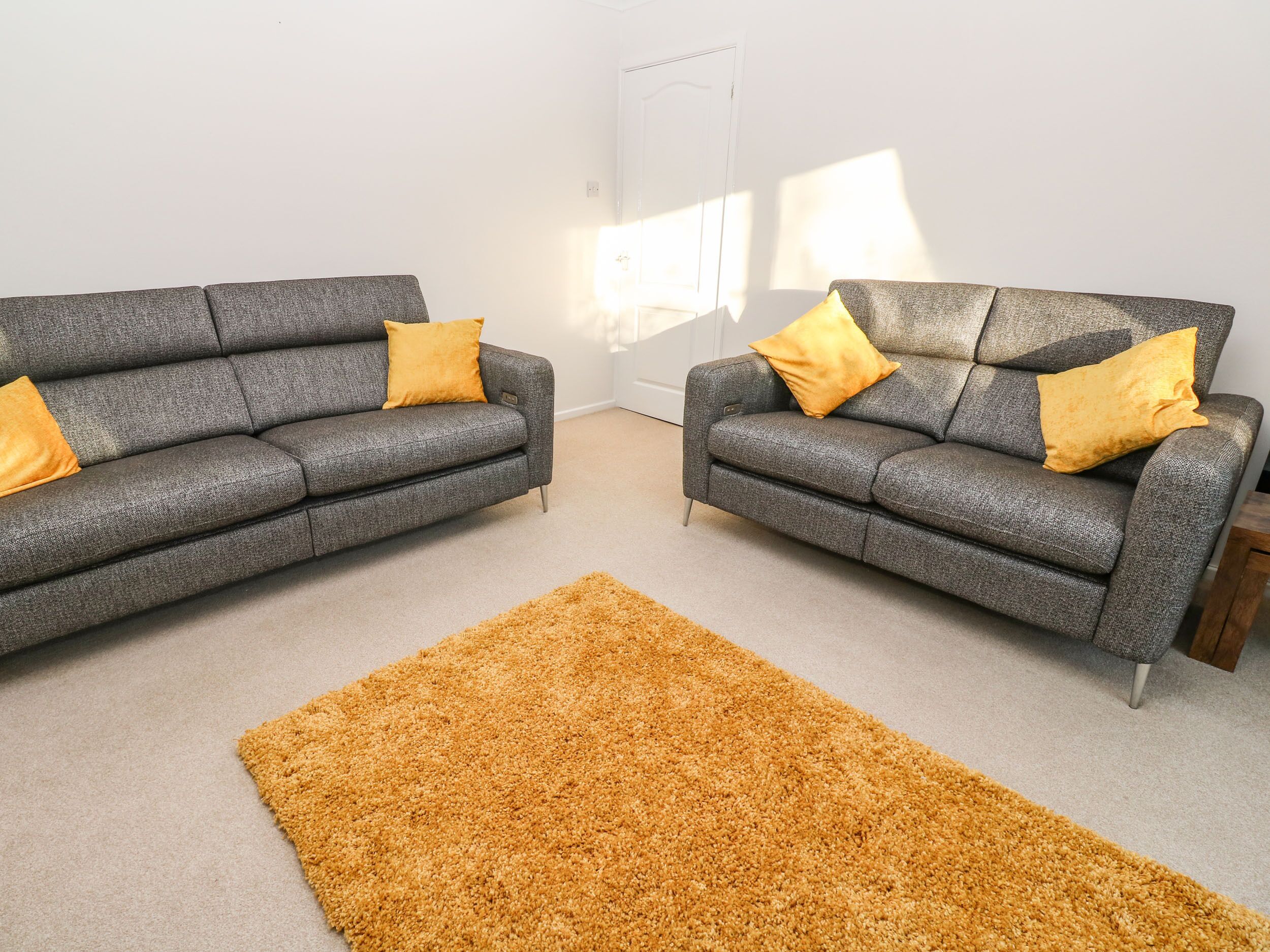 Two grey sofas with yellow cushions, a brown rug, and a white door in a room with light-colored walls.