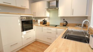 A modern kitchen with white cabinets, a stainless steel oven, a coffee maker, and a sink. - Dunes View (Newquay)