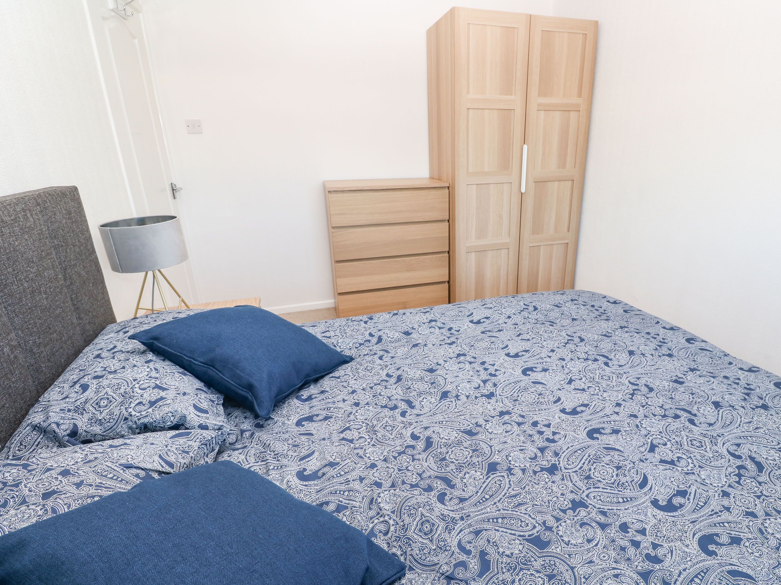 A bedroom with a bed, a nightstand, a lamp, and a wardrobe.