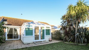 A conservatory with a glass roof, a brick house, and a well-maintained lawn. - Dunes View (Newquay)