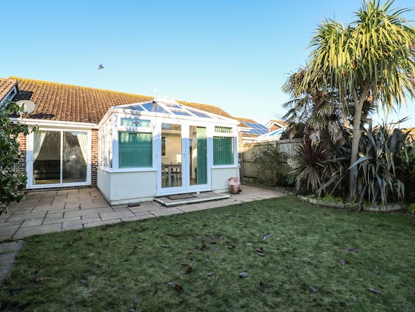 A conservatory with a glass roof, a brick house, and a well-maintained lawn.