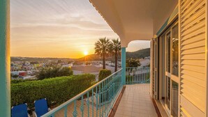 A balcony with a view of a sunset over a residential area, including palm trees and houses. - Villa Loria - beautiful panoramic views (Albufeira)