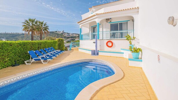 A swimming pool with blue lounge chairs, a lifebuoy, and a view of a hill. - Villa Loria - beautiful panoramic views (Albufeira)