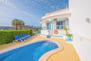 A swimming pool with blue lounge chairs, a lifebuoy, and a view of a hill. - Villa Loria - beautiful panoramic views (Albufeira)