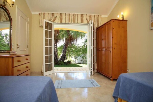 A bedroom with two beds, a wooden wardrobe, and a door leading to a garden.