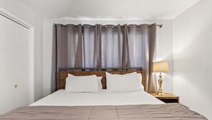 Un letto ben rifatto con una testiera in legno, una lampada da comodino e una finestra con tende.