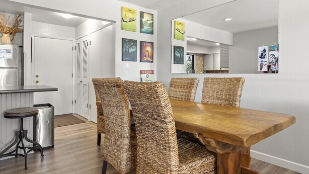 Zona pranzo con tavolo in legno e sedie intrecciate, cucina sullo sfondo e opere d'arte alle pareti.