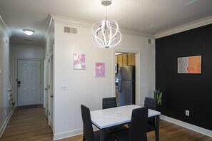 A dining area with a white table and black chairs, a black accent wall, and a modern pendant light.