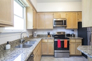 A modern kitchen with granite countertops, stainless steel appliances, wooden cabinets, and a window providing natural light.