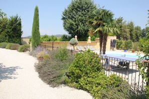 Un jardín con piscina, rodeado por una cerca y diversas plantas y árboles.