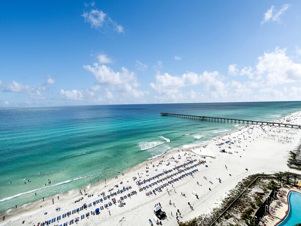 A beach with a pier extending into the ocean, numerous sun loungers, and a clear sky.