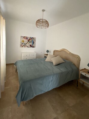 A bedroom with a bed, a nightstand, a lamp, a wall art piece, and a hanging light fixture.