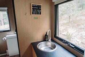 A compact bathroom with a sink, a toilet, and a window offering a view of a wooded area.