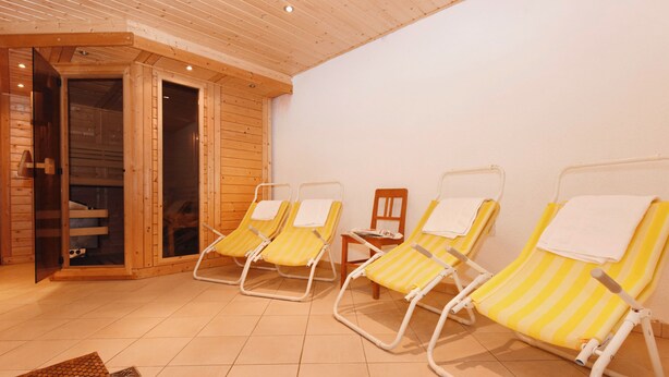 A sauna room with wooden walls and tiled floor, containing four yellow-striped lounge chairs with towels. - Mormenta Ganda, Mormenta Ganda (Gaschurn)