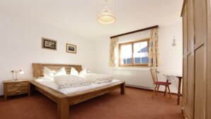 A bedroom with a wooden bed, a nightstand, a chair, and a window with curtains. - Mormenta Ganda, Mormenta Ganda (Gaschurn)