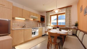 A kitchen with wooden cabinets, a refrigerator, an oven, and a dining area with a table and chairs. - Mormenta Ganda, Mormenta Ganda (Gaschurn)