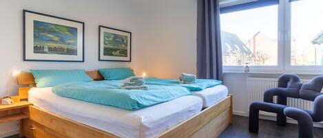 Un dormitorio moderno con una cama de madera, dos cuadros enmarcados de paisajes, una ventana con cortinas y una mesita de noche con lámpara.