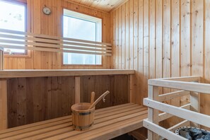 Una sauna de madera con bancos, un balde de madera y una cuchara para servir, y una ventana.