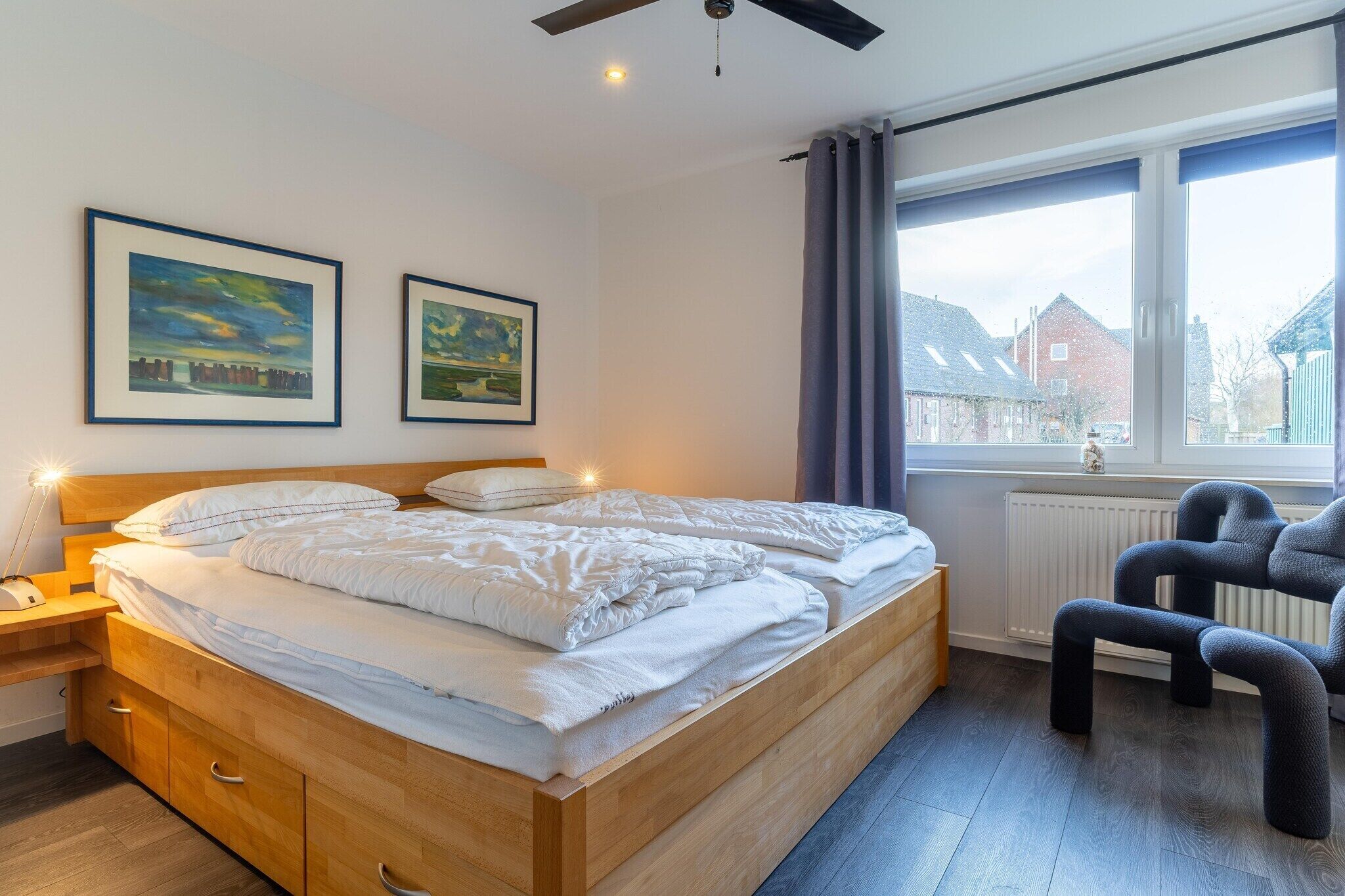 A bedroom with a wooden bed, bedside tables, a chair, and two framed pictures on the wall.