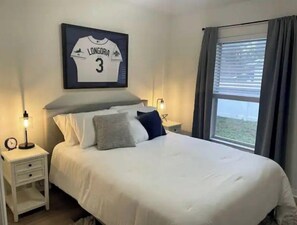 A neatly made bed with a jersey on the wall, two bedside tables, and a window with curtains.