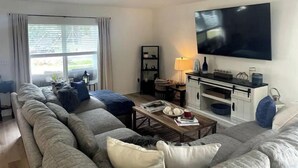 A living room with a large sofa, a coffee table, a TV, and a ceiling fan. - Riverside Riviera at Seminole Heights (Tampa)